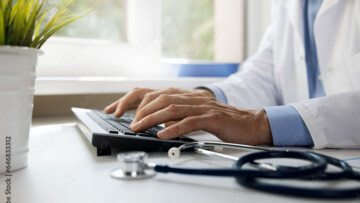 medical professional sitting at his desk, hands typing on his keyboard